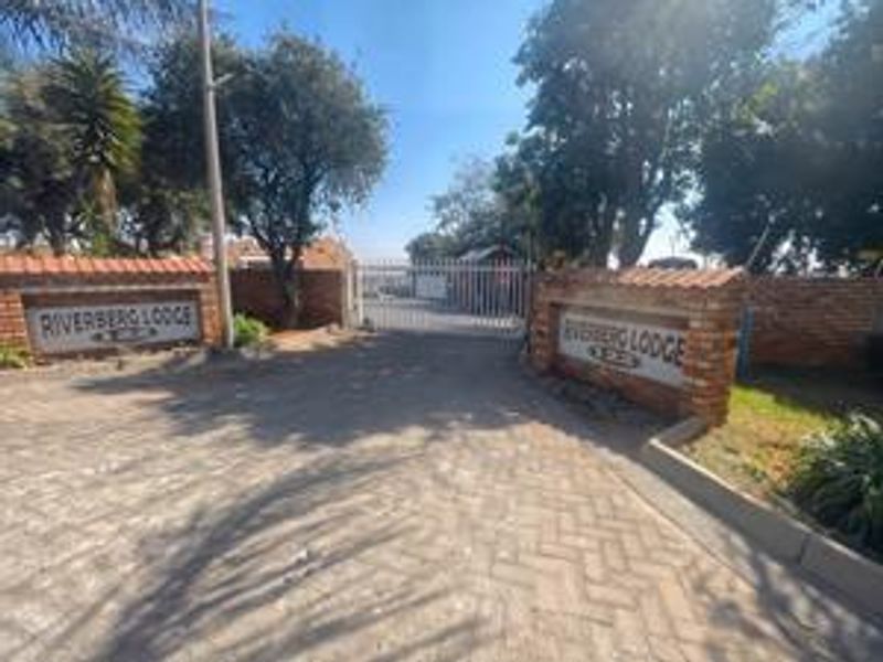 The entrance to Riverberg Lodge featuring a paved driveway, brick boundary walls, and a secure gated access point.