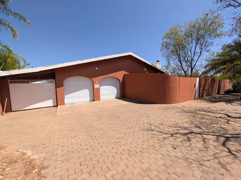 Front elevation of the property featuring a double garage, paved driveway, and secure boundary walling.