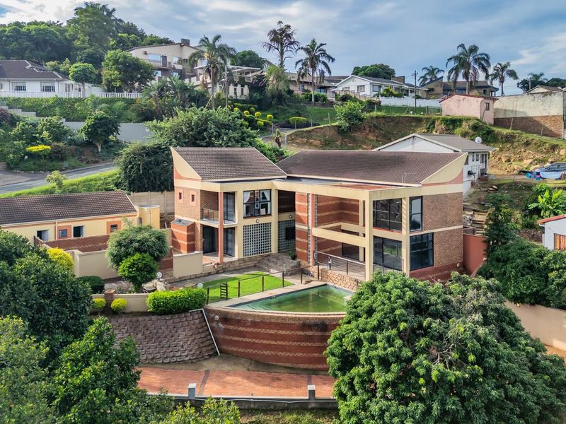 Aerial view of a multi-level residential property featuring a swimming pool, brick exterior, and landscaped grounds in a hillside neighborhood setting.