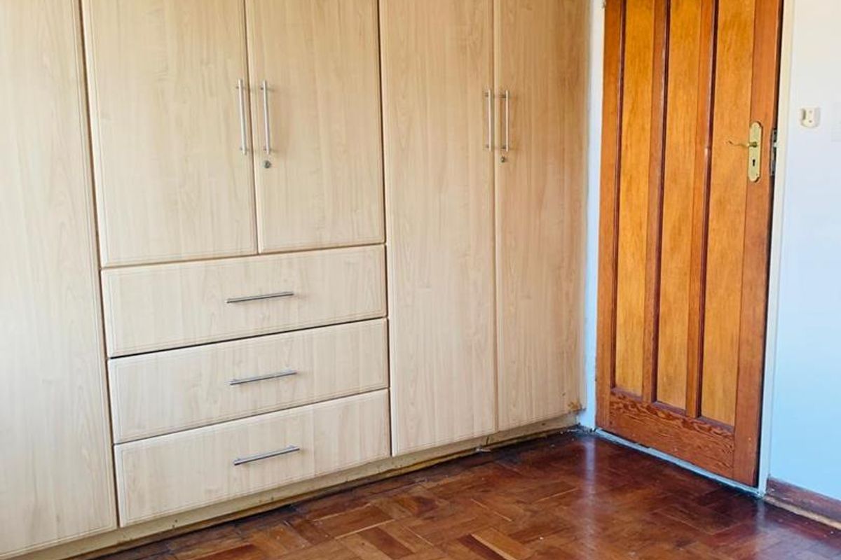 A bedroom featuring extensive light wood built-in cupboards, classic parquet flooring, and a traditional wooden door with a transom window above.