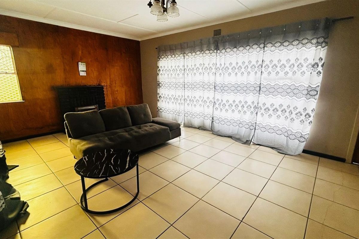 A living room featuring tiled flooring, a built-in fireplace, and wood-paneled accent wall, providing a functional space with potential for modernization.