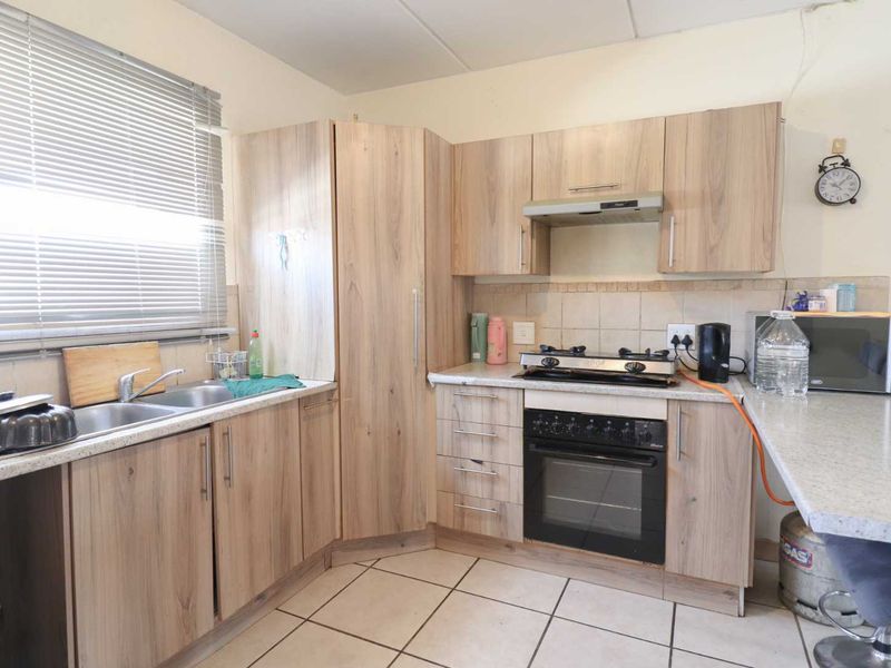 Functional kitchen featuring light wood-look cabinetry, a gas hob with oven, double sink, and tiled flooring with a neutral backsplash.