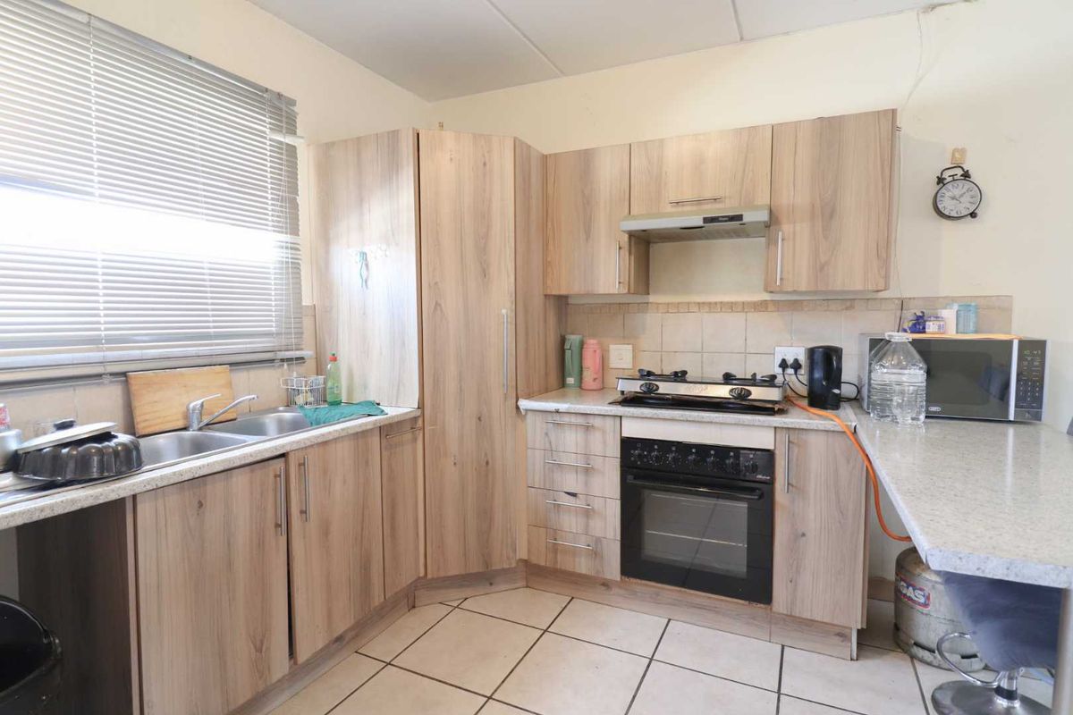 Functional kitchen featuring light wood-look cabinetry, a gas hob with oven, double sink, and tiled flooring with a neutral backsplash.