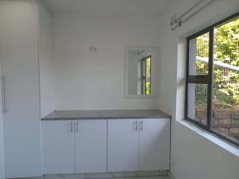 A clean, empty bedroom featuring modern white built-in cabinetry with stone countertops, tiled flooring, and a large window providing natural light.