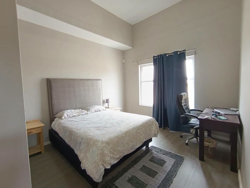 A well-lit bedroom featuring high ceilings, neutral wall tones, and durable laminate flooring, providing a comfortable and spacious living environment.