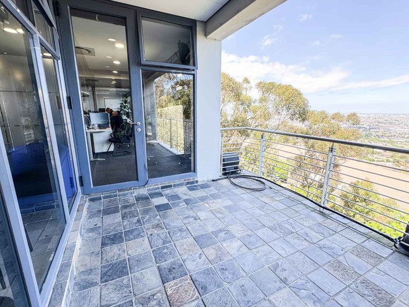 A spacious balcony featuring stone tile flooring, modern metal railings, and expansive views, accessible through large glass doors.