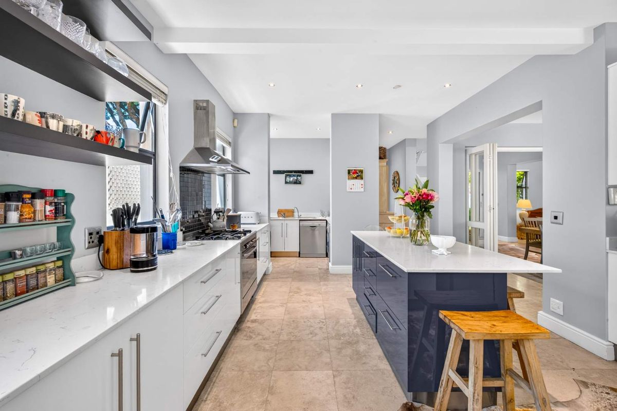 Modern kitchen featuring a central island with stone countertops, stainless steel appliances, gas hob, and tiled flooring, flowing into an adjacent living area.