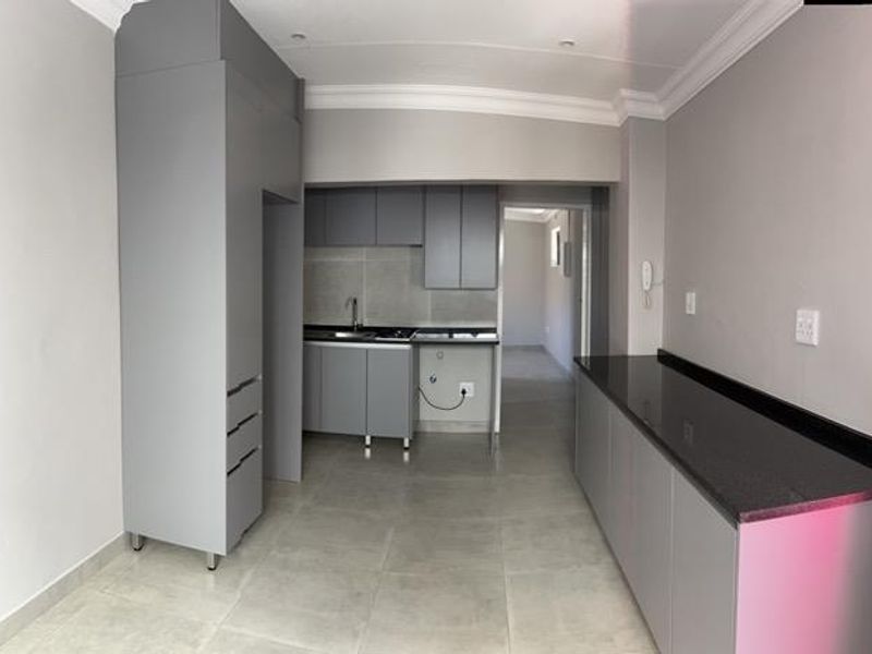A modern, minimalist kitchen featuring grey cabinetry, sleek black granite countertops, tiled flooring, and clean finishes in a bright, open-plan layout.