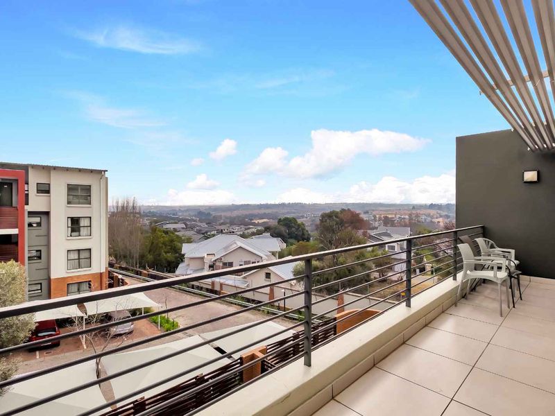 A spacious balcony featuring tiled flooring, a metal balustrade, and a slatted pergola roof, offering expansive views of the surrounding neighbourhood.