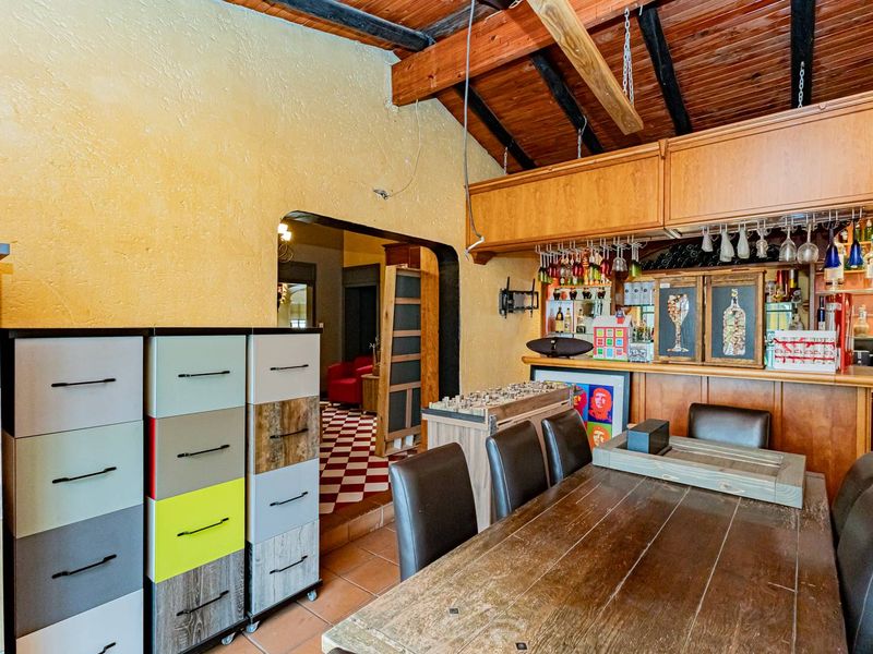 A rustic bar area featuring exposed timber ceiling beams, a built-in bar counter with integrated glassware storage, and traditional tiled flooring.