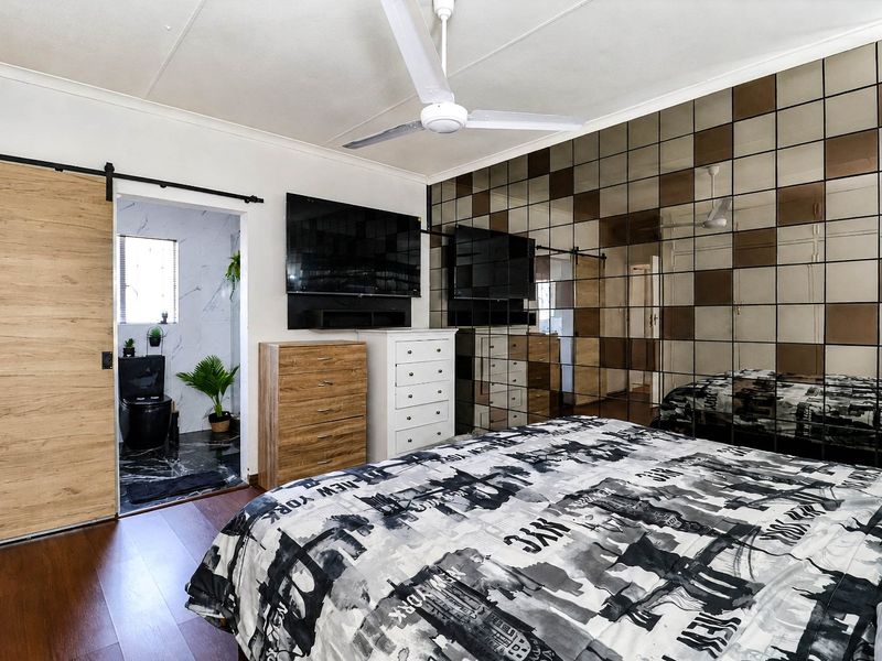 A well-maintained bedroom featuring a modern ceiling fan, a sliding barn door, and a distinctive mirrored feature wall, with an adjoining en-suite bathroom.