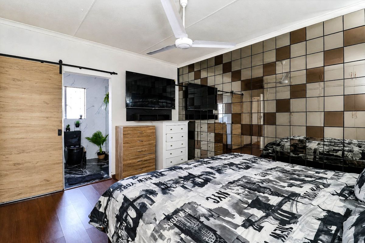 A well-maintained bedroom featuring a modern ceiling fan, a sliding barn door, and a distinctive mirrored feature wall, with an adjoining en-suite bathroom.