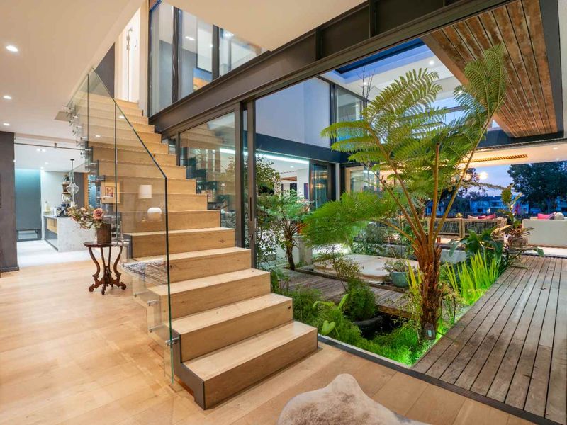 Modern open-plan living area featuring a striking timber staircase with glass balustrade, steel structural elements, and a seamless transition to an internal courtyard garden.