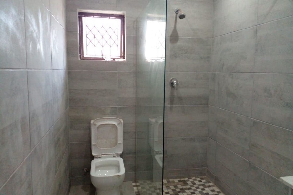 A modern bathroom featuring grey wall tiles, a glass shower enclosure, mosaic floor tiling, and a security-grille window.