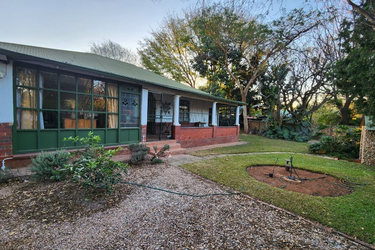 Rear view of the house featuring a covered veranda, brick facade, metal roofing, and a spacious garden area with stone pathways.