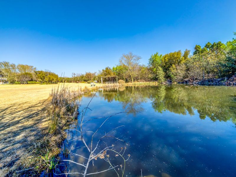 A scenic view of a tranquil pond surrounded by mature trees and well-maintained landscaped grounds within the residential estate.