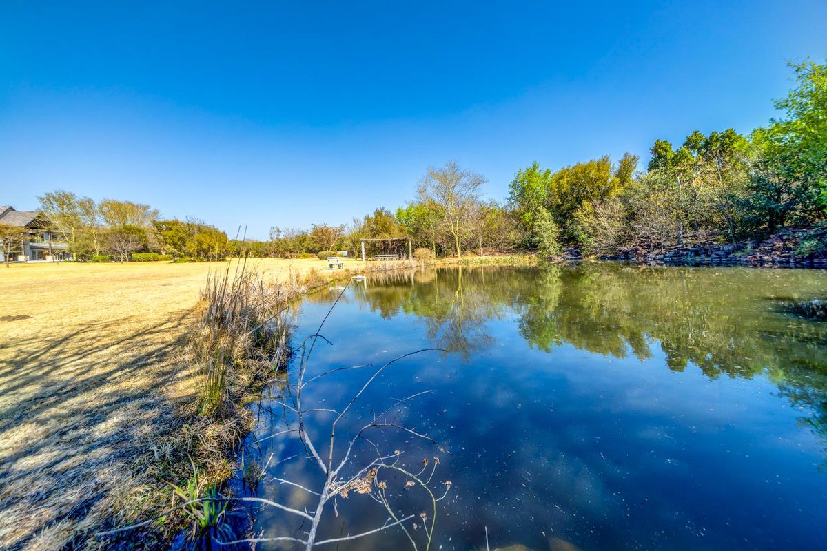 A scenic view of a tranquil pond surrounded by mature trees and well-maintained landscaped grounds within the residential estate.