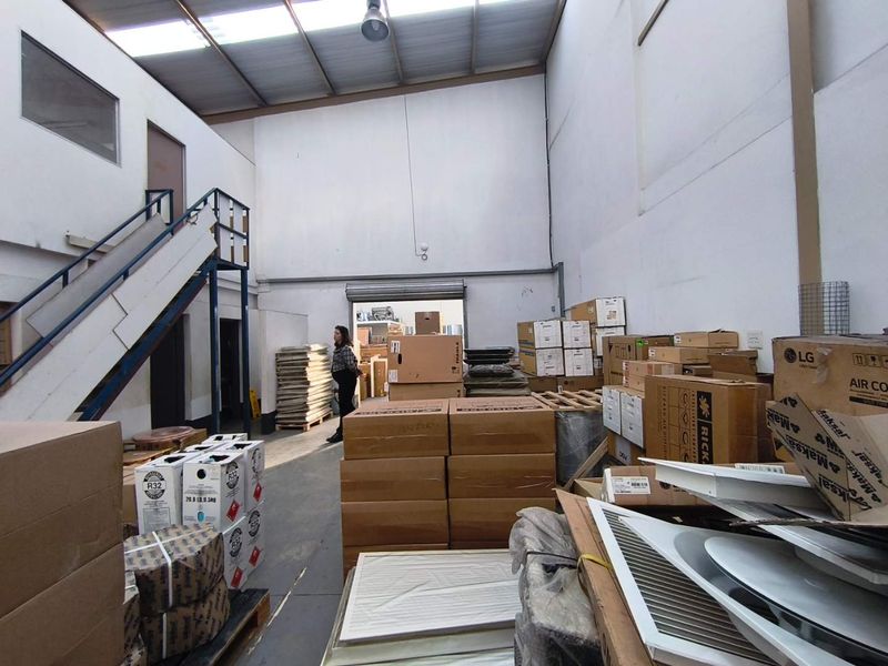 Industrial warehouse space featuring high ceilings, a metal staircase, and a large roller shutter door for efficient loading and access.