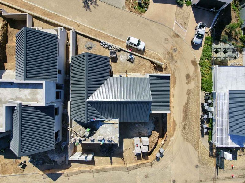 Aerial view of a residential property under construction, showing the roof structure, paved driveway, and surrounding site development.
