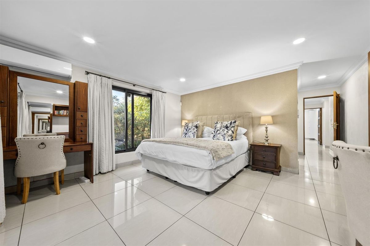 Spacious bedroom featuring large format floor tiles, recessed downlighting, and a wall-mounted air conditioning unit, offering a bright and comfortable living space.
