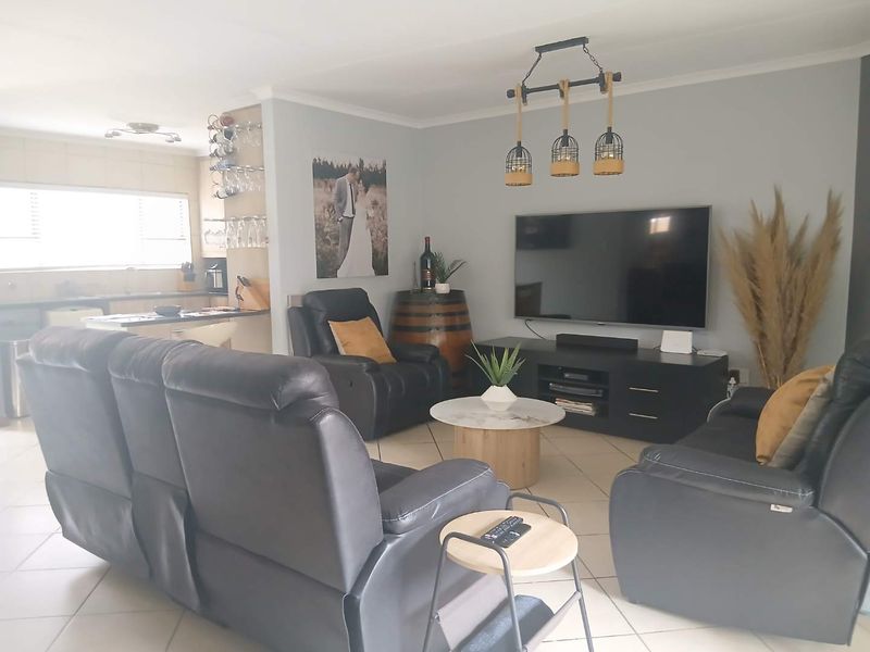 An open-plan living area featuring tiled flooring, integrated kitchen cabinetry, and modern pendant lighting, creating a functional and connected living and kitchen space.