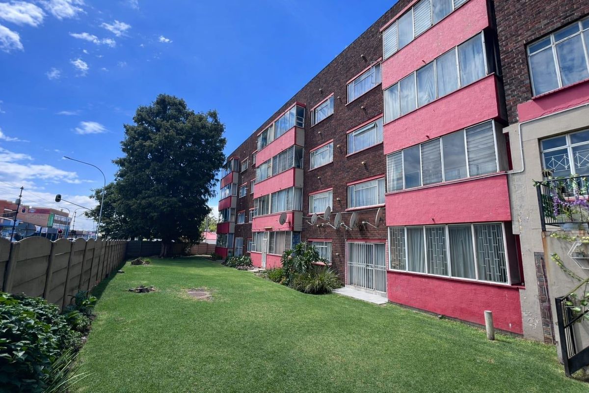 A view of the rear exterior of a multi-story apartment building featuring brick and painted facade elements, overlooking a shared lawn area.