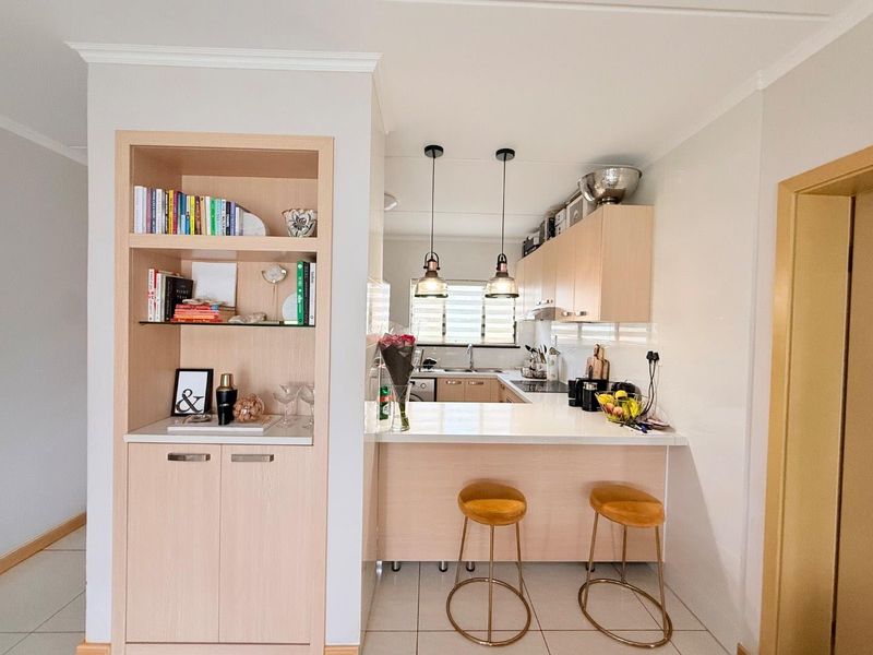 A well-maintained kitchen featuring light wood cabinetry, stone countertops, a breakfast bar, and integrated shelving, creating a functional and modern open-plan space.