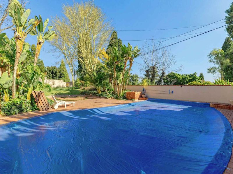 Outdoor pool area featuring a large swimming pool with a cover, surrounded by brick paving and established garden landscaping.