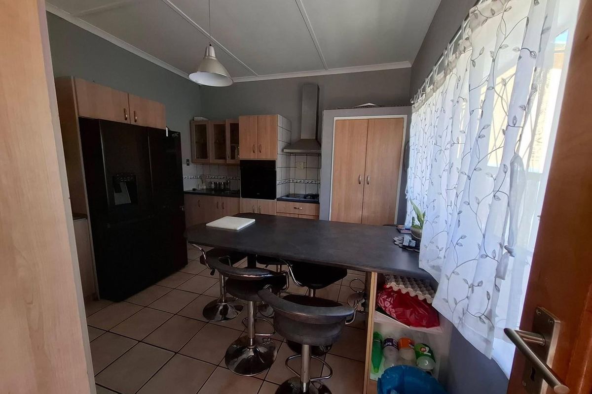 A functional kitchen featuring built-in cabinetry, a breakfast bar, tiled flooring, and integrated appliances including an oven and extractor fan.