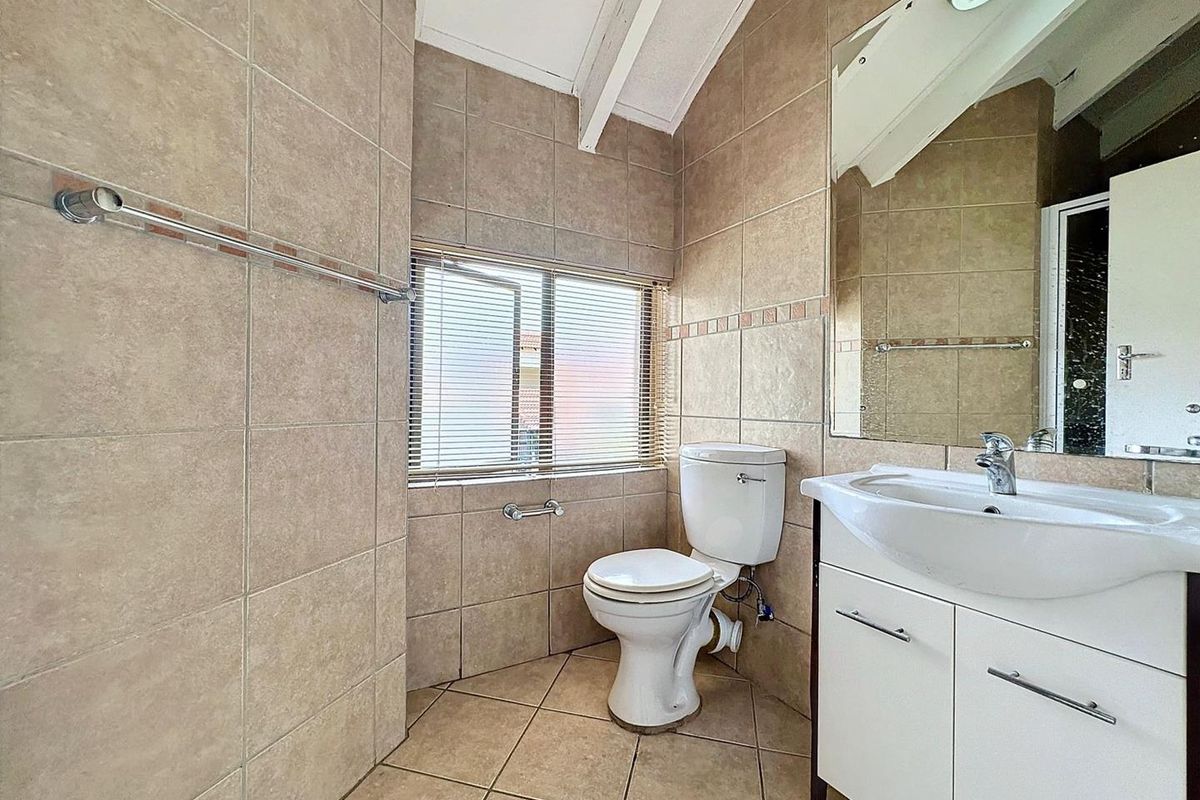 A functional bathroom featuring tiled walls and flooring, a white vanity cabinet with a basin, a toilet, and a large wall-mounted mirror.