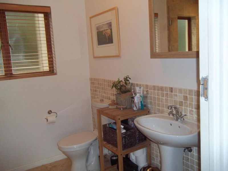 A functional bathroom featuring a pedestal sink, toilet, and neutral tiled splashback, complemented by a wall-mounted mirror and natural light from the window.