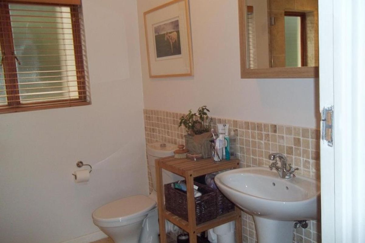 A functional bathroom featuring a pedestal sink, toilet, and neutral tiled splashback, complemented by a wall-mounted mirror and natural light from the window.