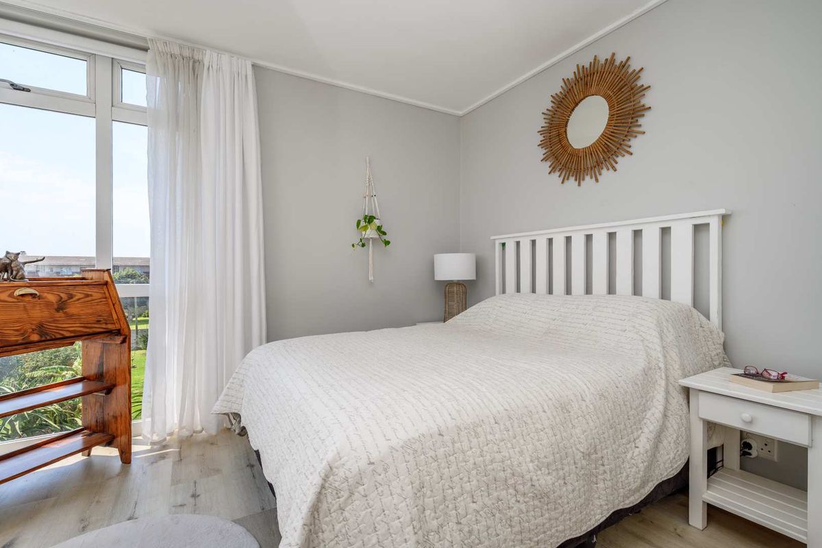 A bright and well-maintained bedroom featuring light-toned laminate flooring and a large window that allows for ample natural light.