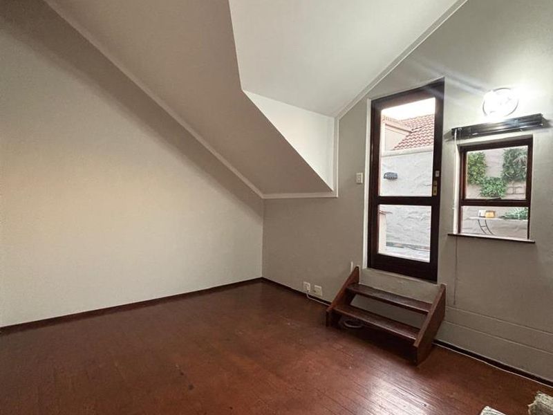 An empty bedroom featuring timber flooring, a sloped ceiling, and direct access to an outdoor area via a glass panel door.