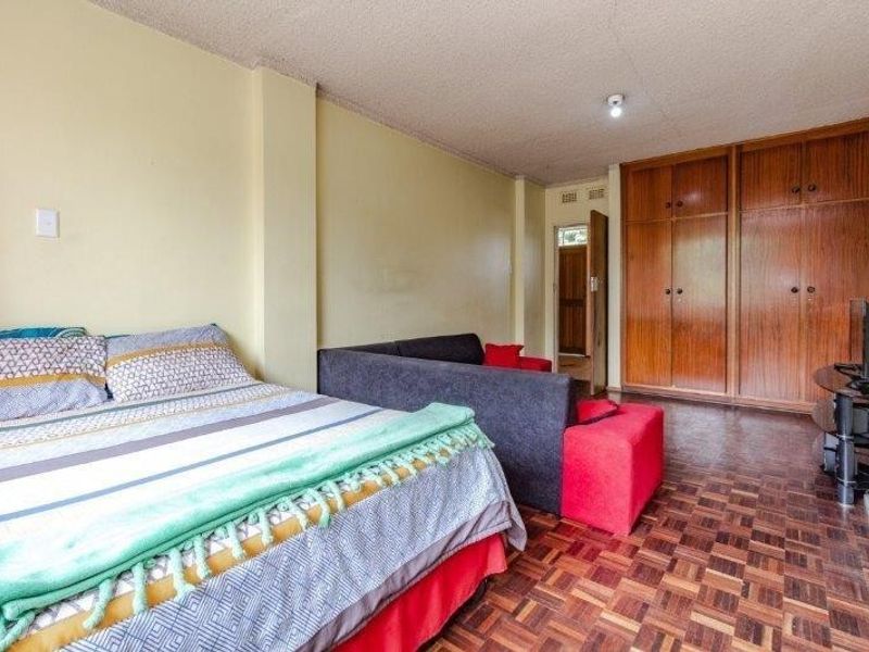 Spacious bedroom featuring classic parquet flooring, textured ceilings, and extensive built-in wooden cabinetry for ample storage.