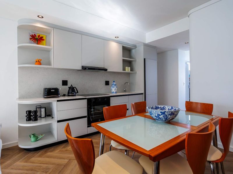 Modern open-plan kitchen and dining area featuring sleek white cabinetry, integrated appliances, and stylish herringbone flooring.