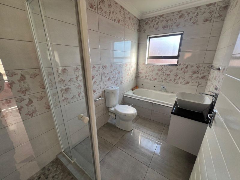 A functional bathroom featuring a shower enclosure, bathtub, toilet, and a modern vessel sink set on a vanity cabinet with tiled finishes.