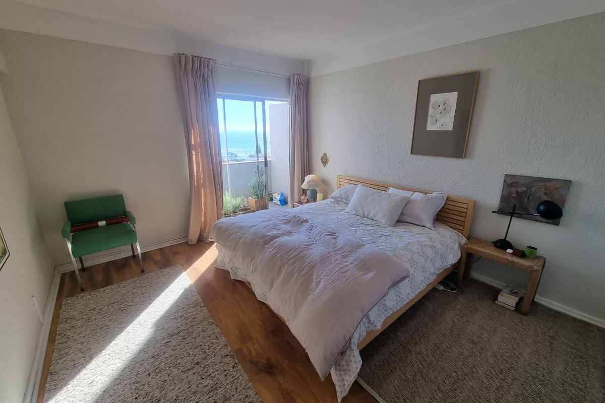 A bright bedroom featuring laminate flooring, coved ceilings, and a sliding glass door that opens to a balcony with ocean views.