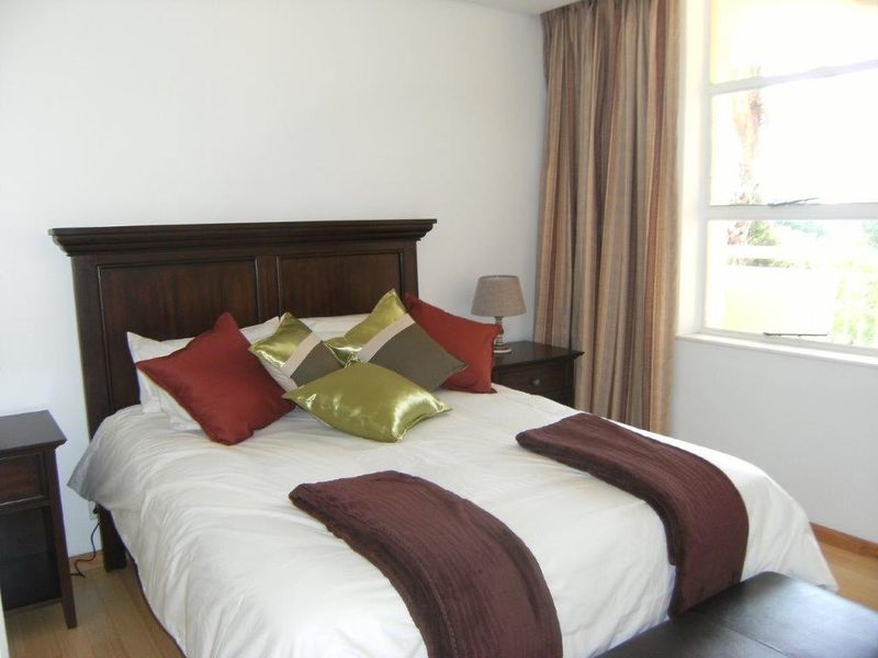 A well-lit bedroom featuring laminate flooring and a large window with curtains, providing a comfortable and functional living space.