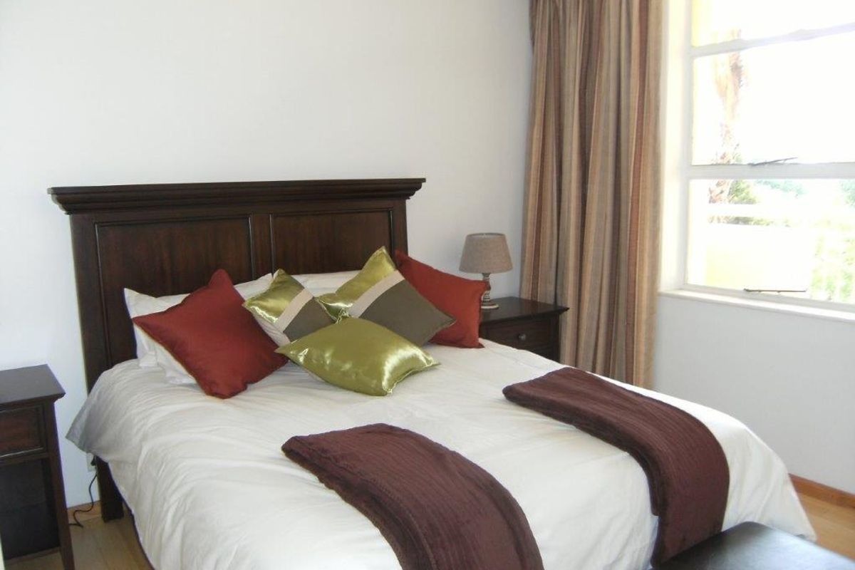 A well-lit bedroom featuring laminate flooring and a large window with curtains, providing a comfortable and functional living space.