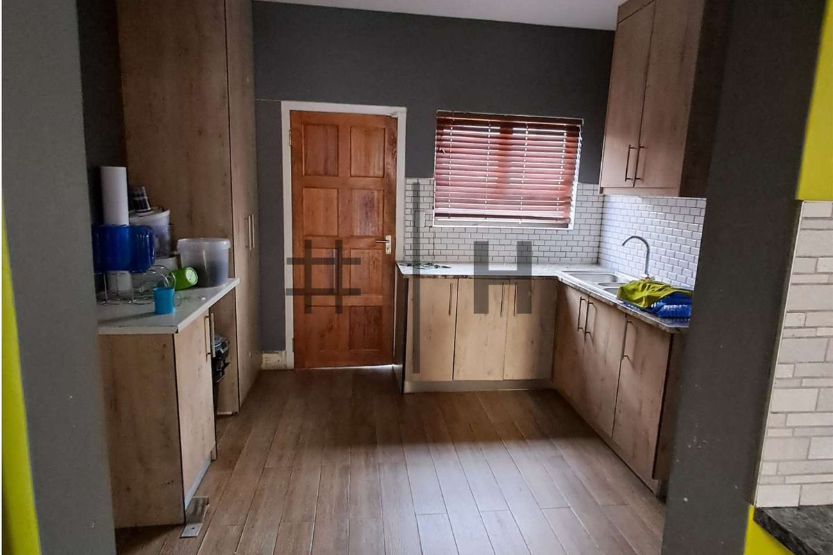 A functional kitchen featuring wood-look cabinetry, subway tile backsplash, stainless steel sink, and wood-style flooring with a wooden door leading outside.