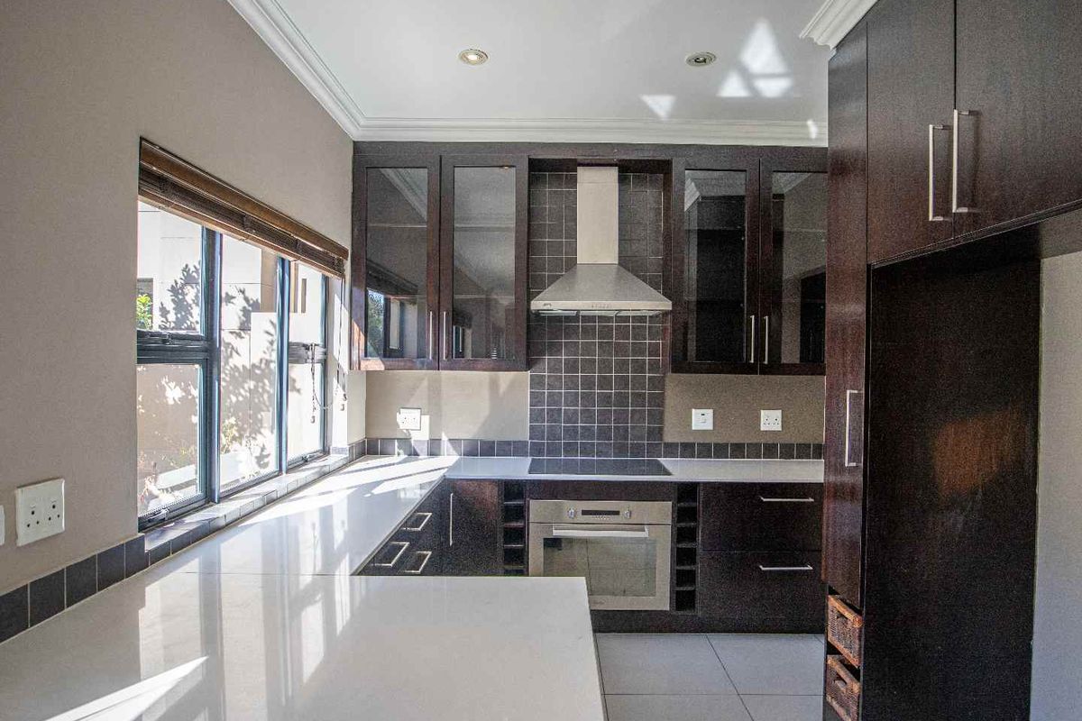 Modern kitchen featuring dark wood cabinetry, stone countertops, built-in oven, electric cooktop, and stainless steel extractor fan.