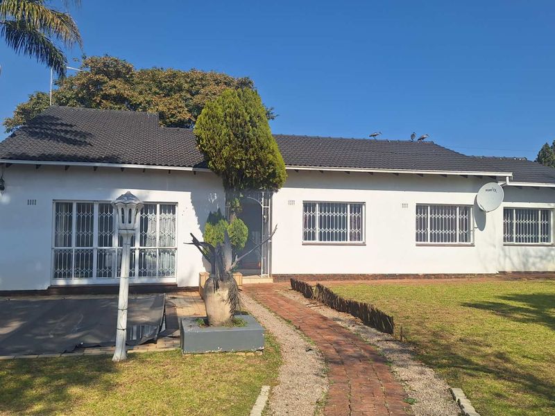 Rear view of a single-story house featuring a tiled roof, white facade, security bars on windows, and a brick pathway leading to the entrance.