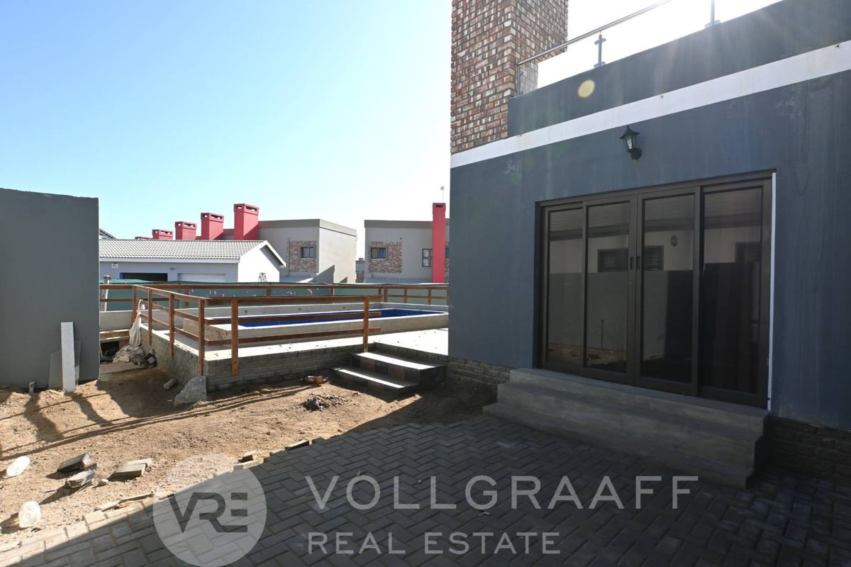 Rear exterior view featuring a paved patio, sliding glass doors, and a raised swimming pool area with timber railing.