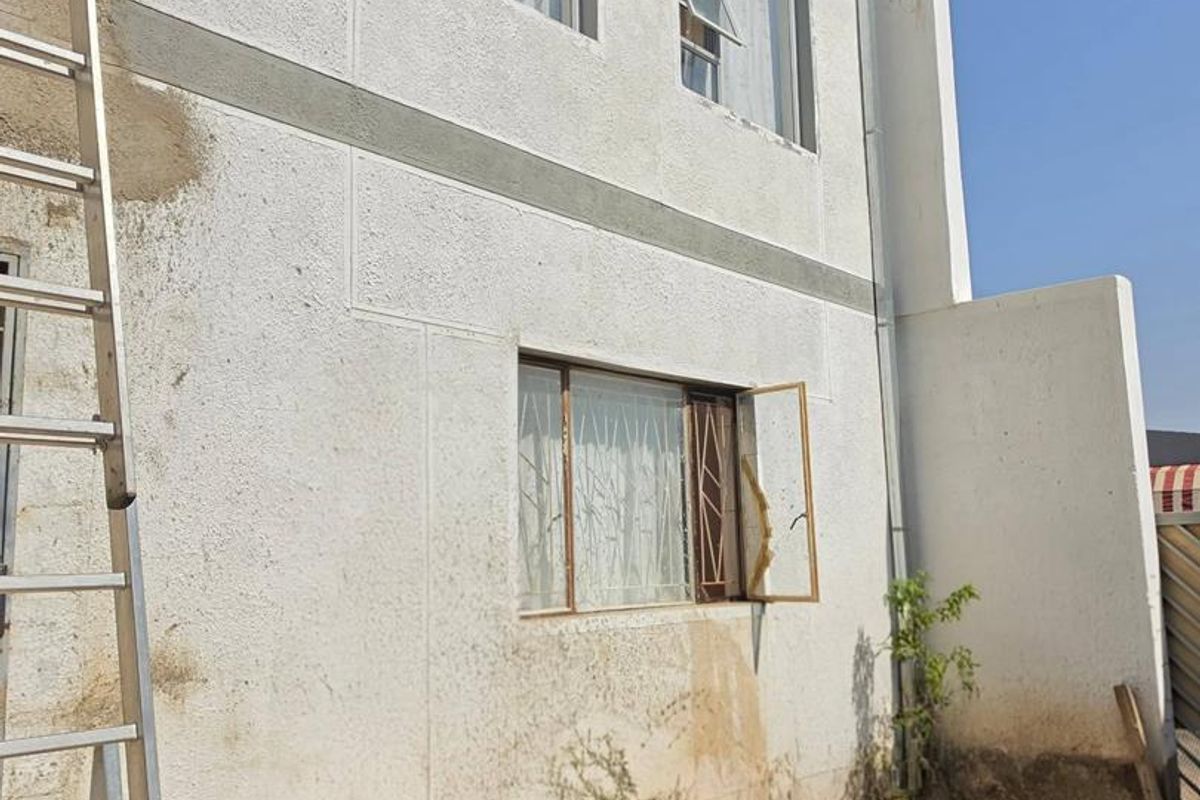 Rear exterior view of a two-story house showing textured wall finishes, aluminium windows, and an unpaved ground area.