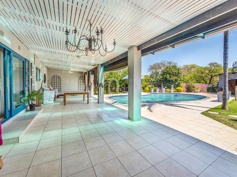 Spacious covered patio featuring tiled flooring and a slatted ceiling, overlooking a private swimming pool and landscaped garden area.