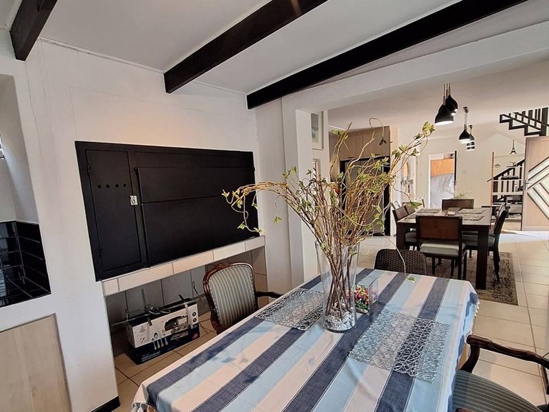 Dining area featuring exposed ceiling beams, tiled flooring, and a built-in braai, creating a functional space that flows into the adjacent living area.
