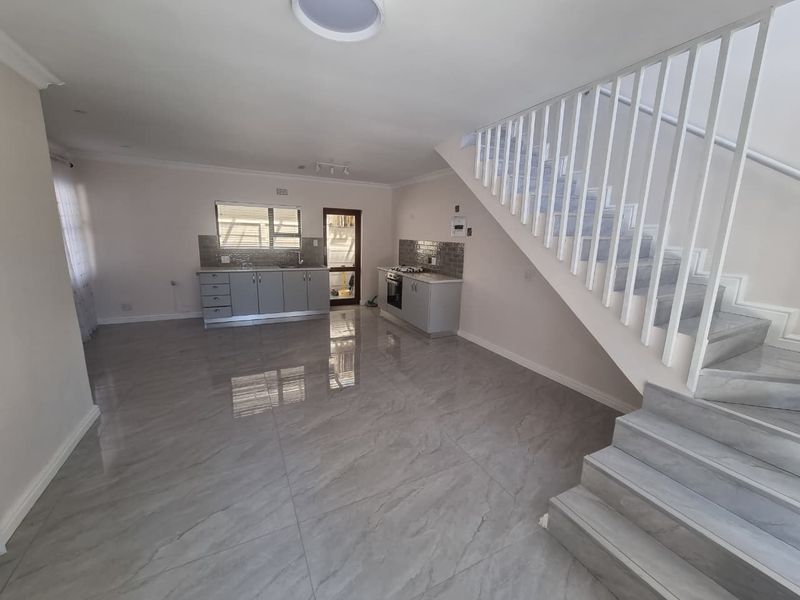 Spacious open-plan living area featuring modern grey tiled flooring, a sleek kitchen with built-in appliances, and a contemporary staircase.