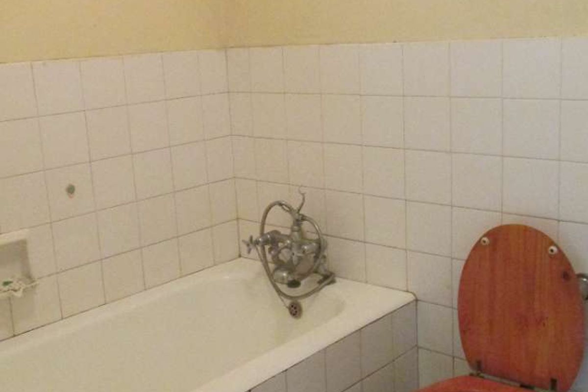 A dated bathroom featuring a built-in bathtub with wall-mounted taps, a standard toilet, and a wall-mounted drying rack.