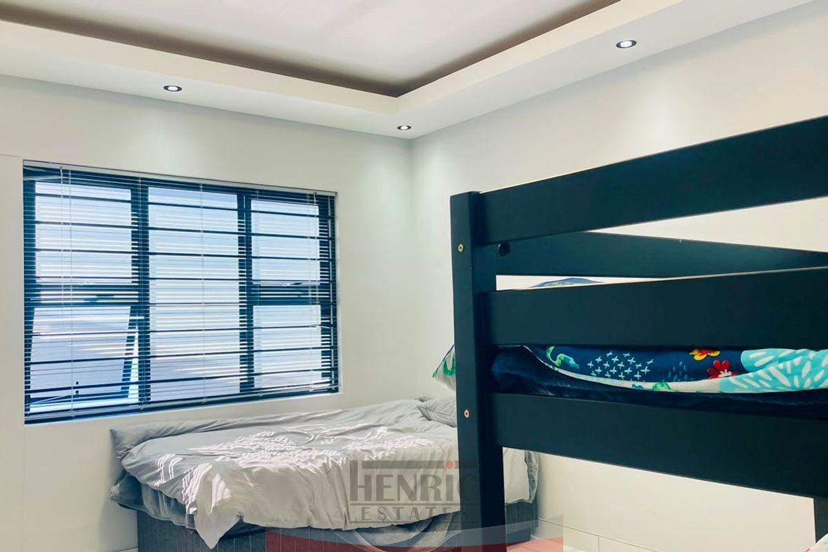A well-lit bedroom featuring a modern bulkhead ceiling with recessed lighting and large aluminium-framed windows.